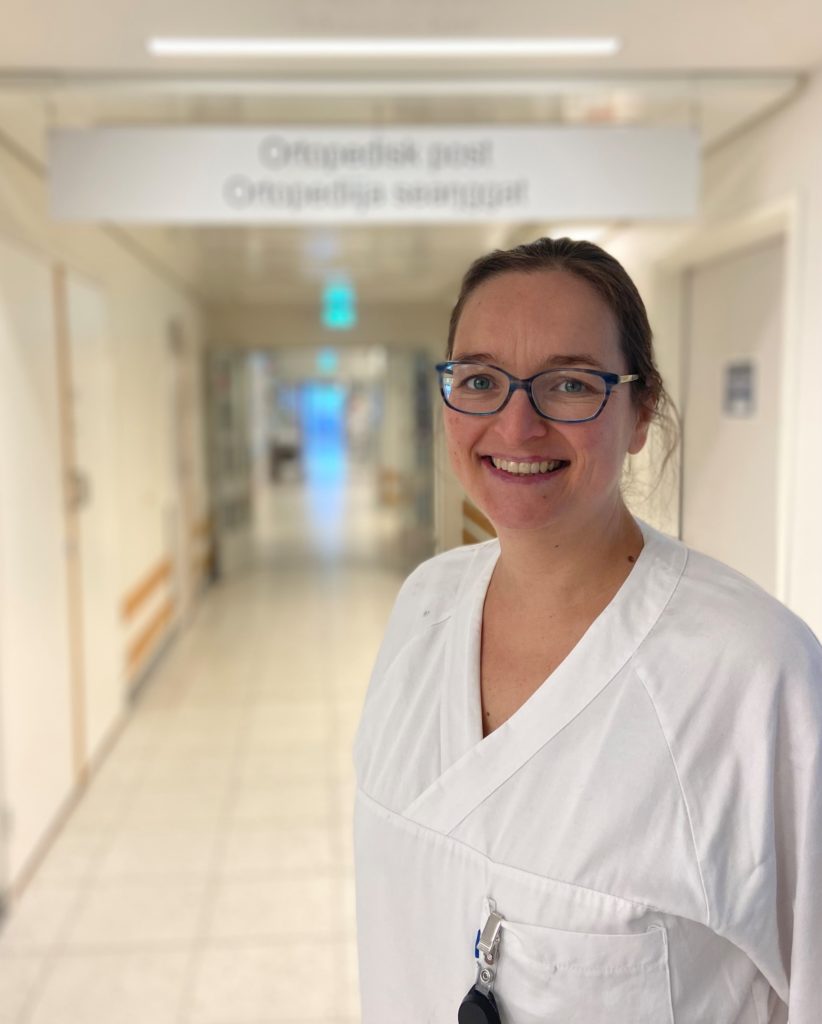 Helsearbeider kledd i hvitt som står i en sykehusgang og smiler